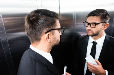 Asansörde aynaya bakan takım elbiseli iş adamının yüksek açılı görüntüsü