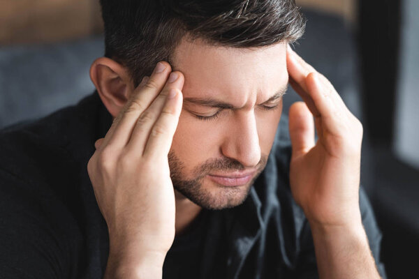 handsome man with headache touching head in apartment 