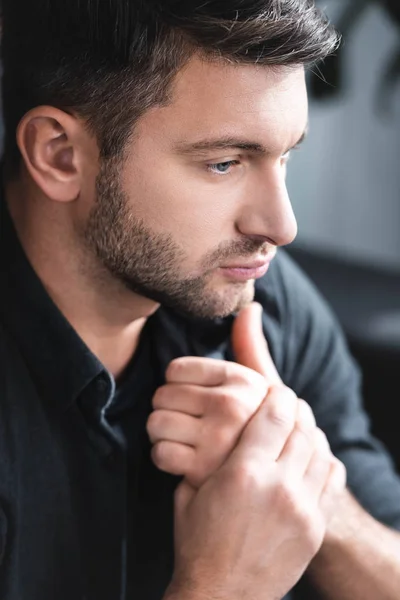 handsome and pensive man in black shirt looking away in apartment