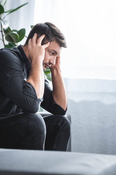 вид сбоку на красивого человека с головой, сидящего на диване в квартире
 