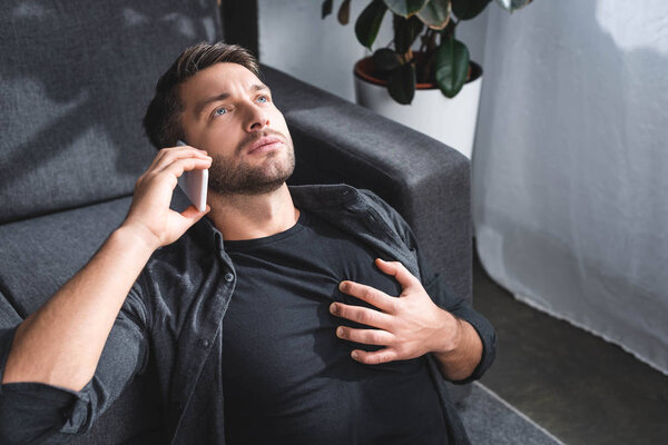 high angle view of handsome man having heart attack and talking on smartphone in apartment 