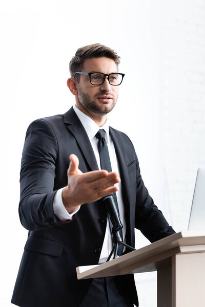 бизнесмен в костюме, стоящий на трибуне и выступающий во время конференции изолированный по белому
