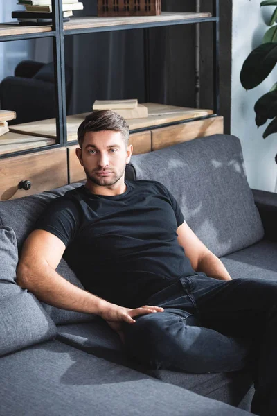 Όμορφος Άντρας Μαύρο Μπλουζάκι Κάθεται Στον Καναπέ Στο Διαμέρισμα — Φωτογραφία Αρχείου
