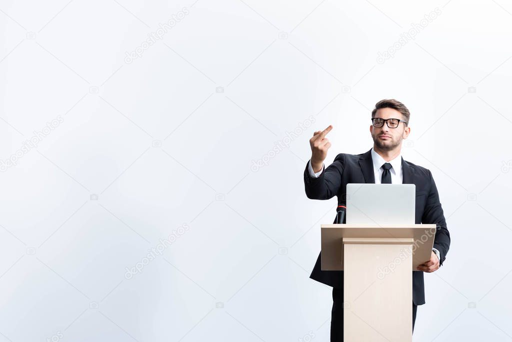 businessman in suit standing at podium tribune and showing middle finger during conference isolated on white