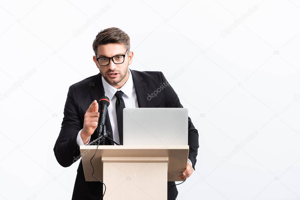 businessman in suit standing at podium tribune and pointing with finger during conference isolated on white