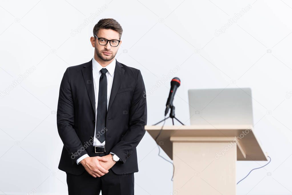 selective focus of scared businessman in suit standing near podium tribune during conference isolated on white