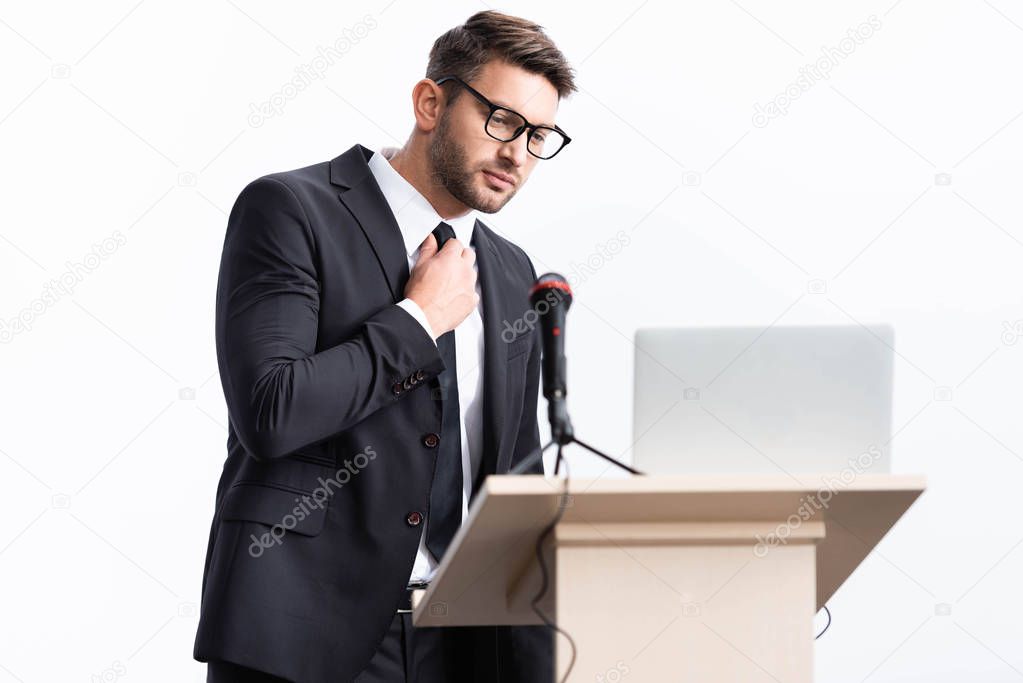 scared businessman in suit standing at podium tribune and touching tie during conference isolated on white