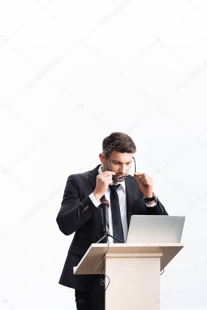 businessman in suit standing at podium tribune and wearing glasses during conference isolated on white