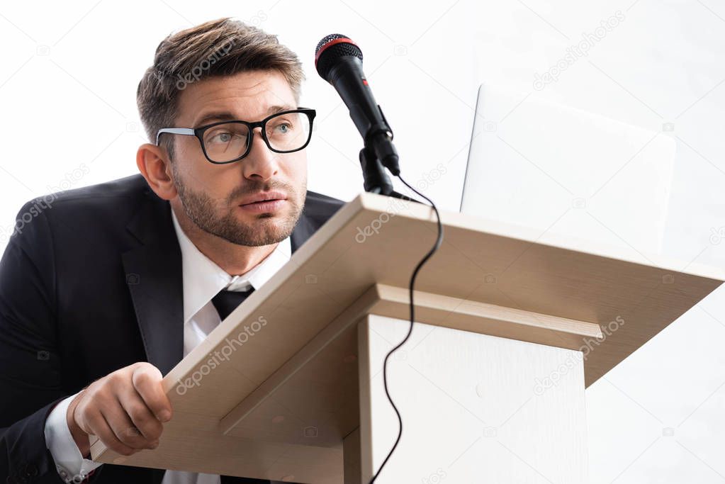 scared businessman in suit standing at podium tribune during conference isolated on white