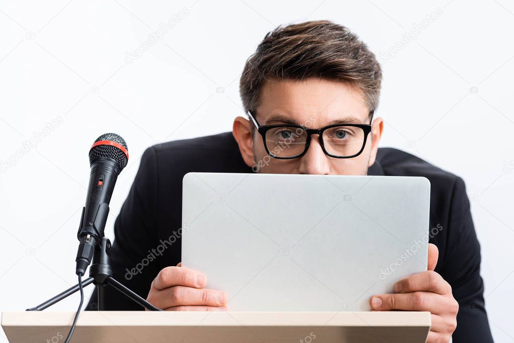 scared businessman in suit hiding behind laptop during conference isolated on white