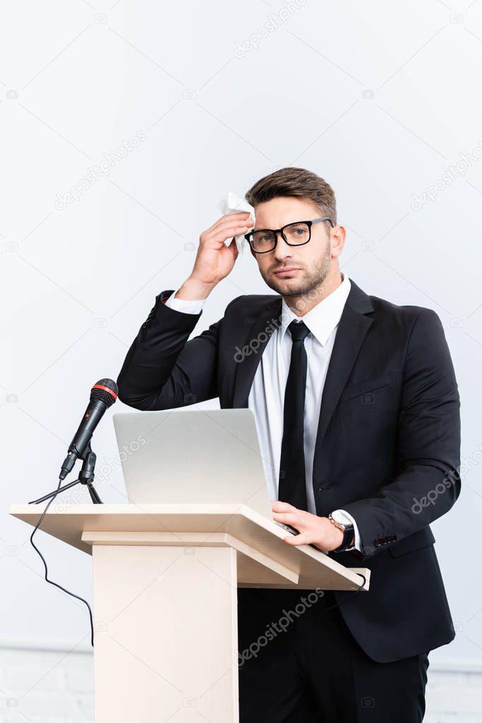 scared businessman in suit standing at podium tribune and holding napkin during conference isolated on white 