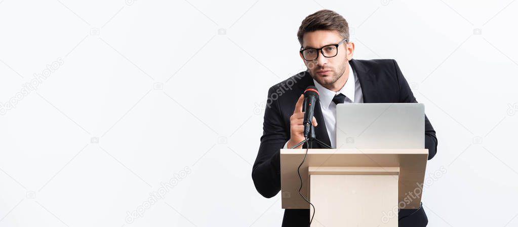 panoramic shot of businessman in suit standing at podium tribune and speaking during conference isolated on white 