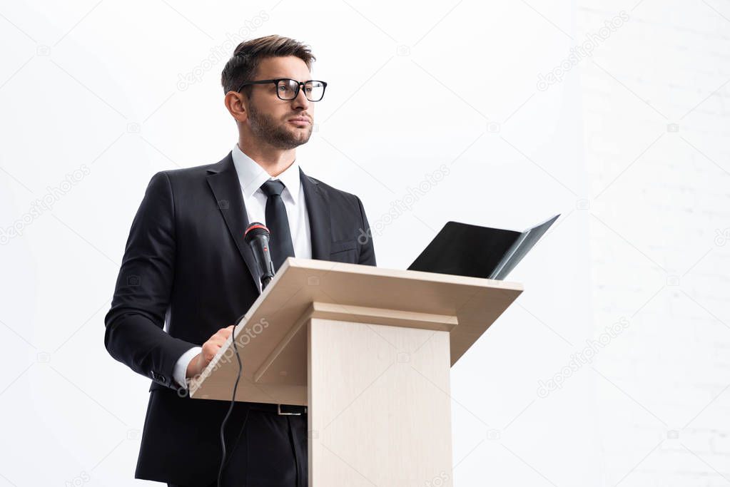 businessman in suit standing at podium tribune and looking away during conference isolated on white 