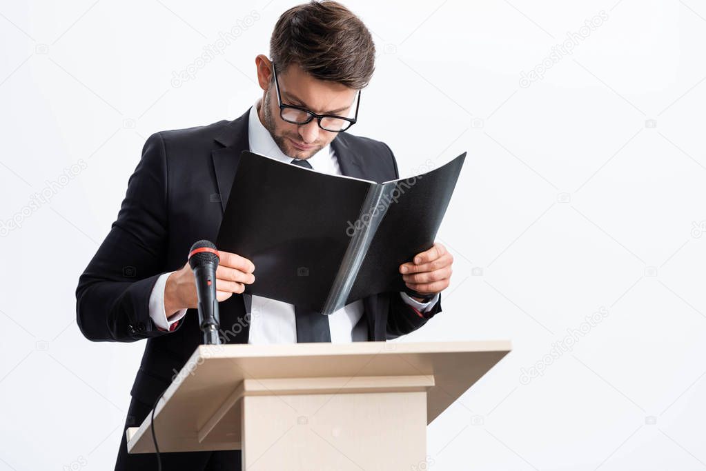 businessman in suit standing at podium tribune and holding folder during conference isolated on white 