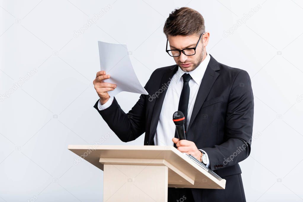 scared businessman in suit standing at podium tribune and holding microphone during conference isolated on white 
