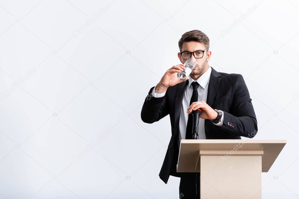 scared businessman in suit standing at podium tribune and drinking water during conference isolated on white 