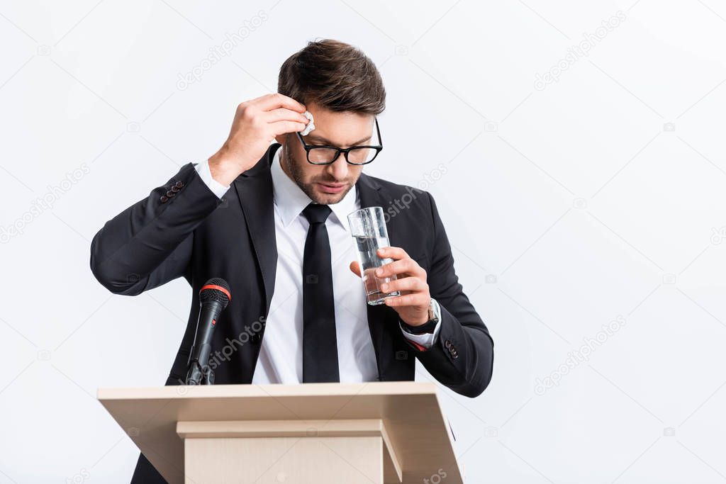 scared businessman in suit standing at podium tribune and holding glass of water during conference isolated on white 