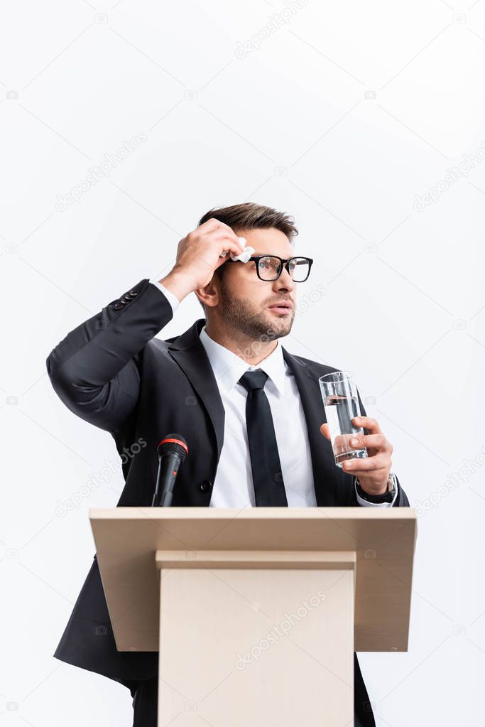 scared businessman in suit standing at podium tribune and holding glass of water during conference isolated on white 