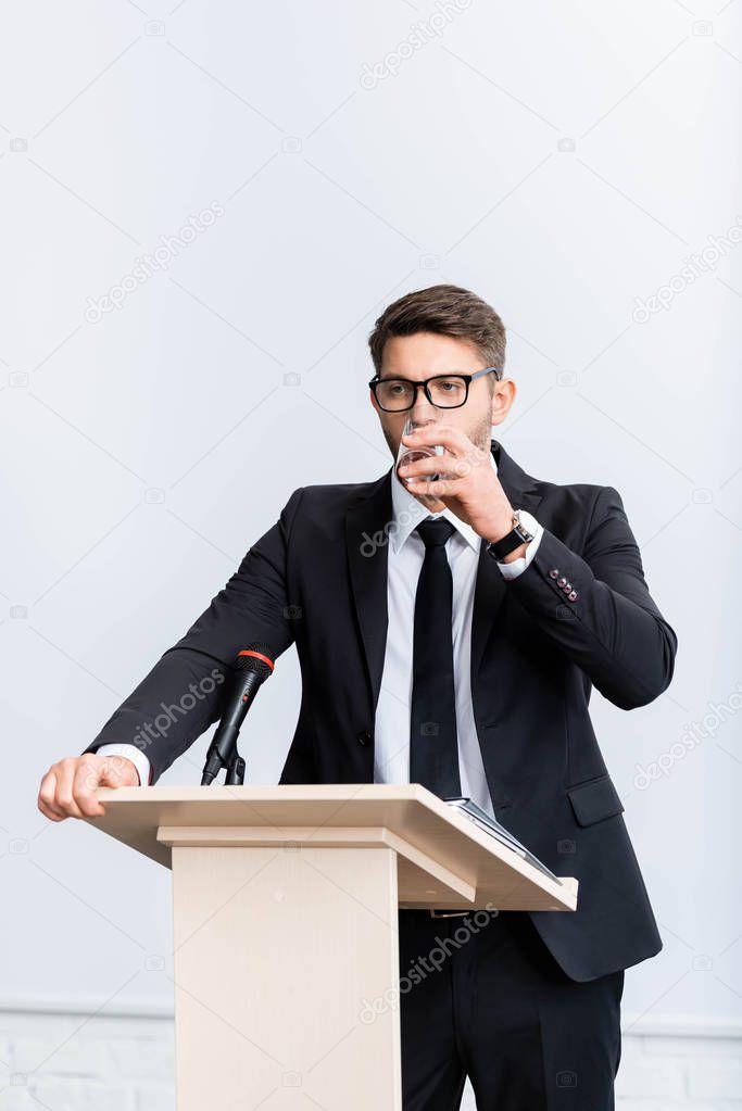 scared businessman in suit standing at podium tribune and drinking water during conference isolated on white