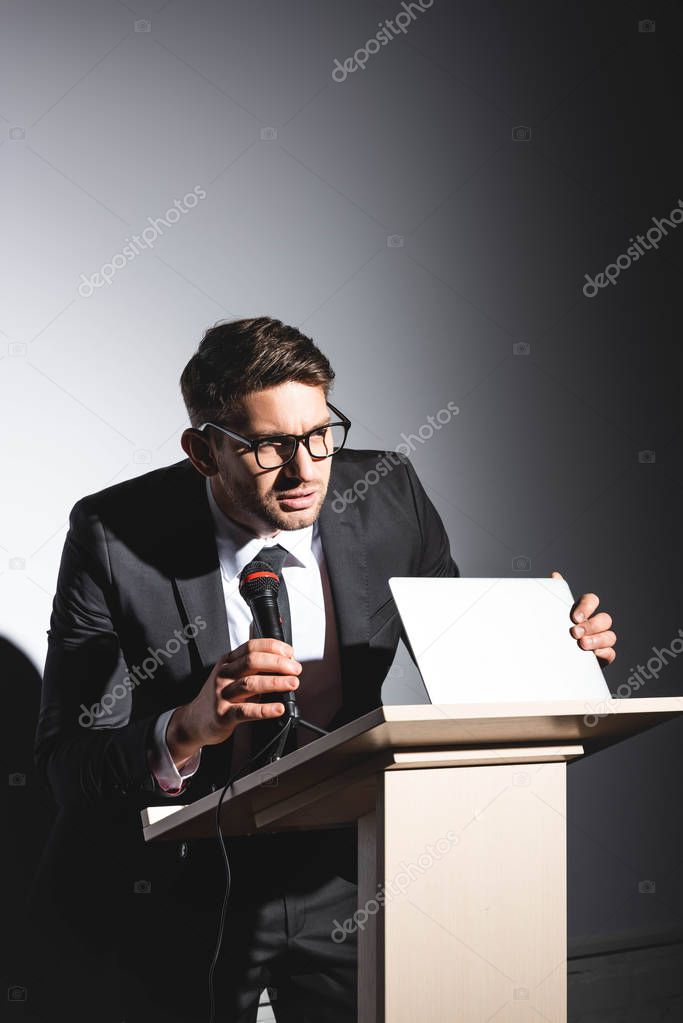 scared businessman in suit standing at podium tribune and holding laptop during conference on white background 