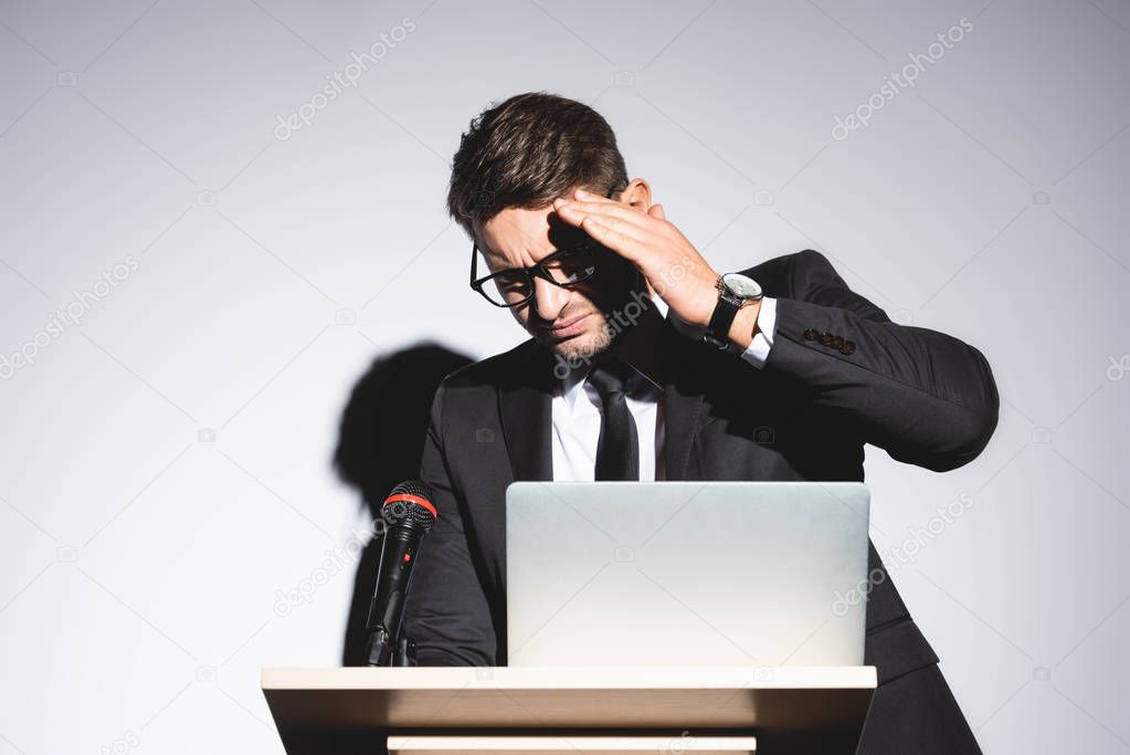scared businessman in suit standing at podium tribune and obscuring face during conference on white background 