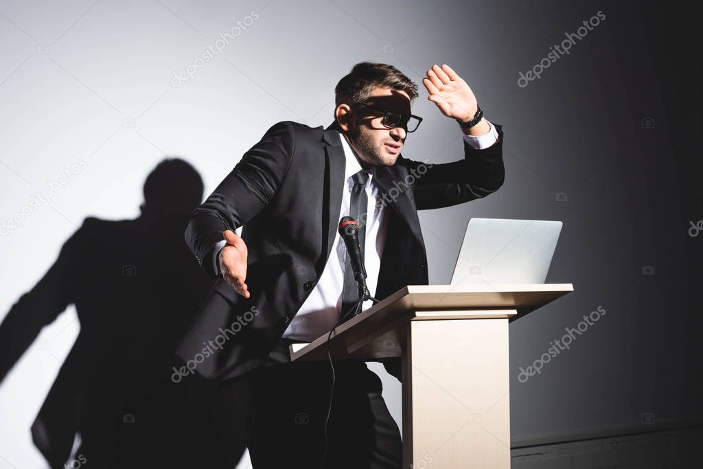 scared businessman in suit standing at podium tribune and obscuring face during conference on white background 