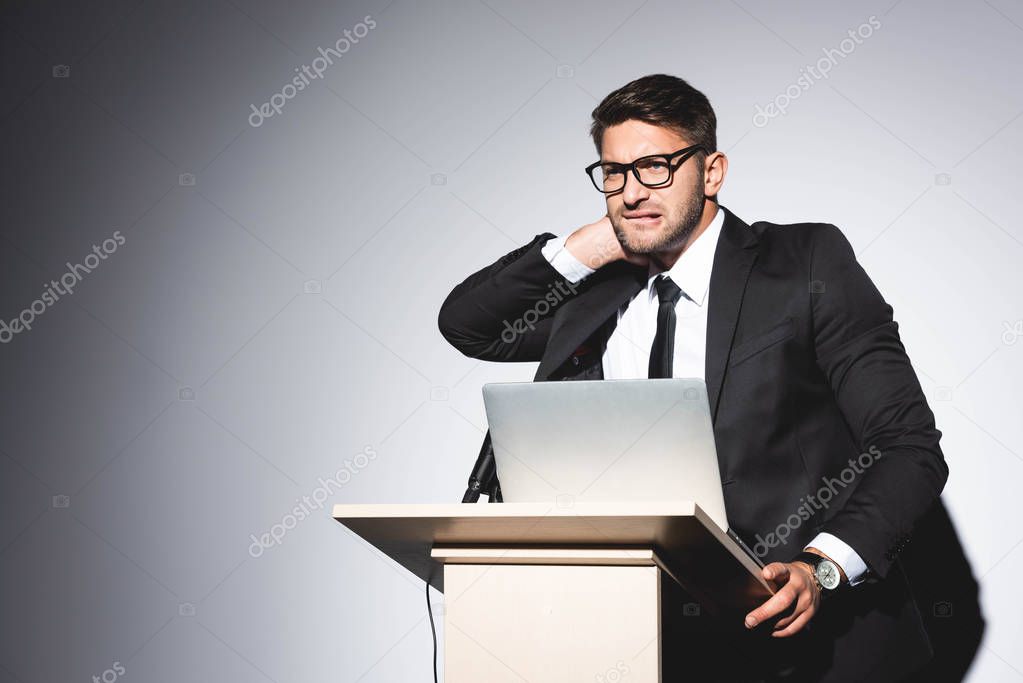 scared businessman in suit standing at podium tribune and looking away during conference on white background 