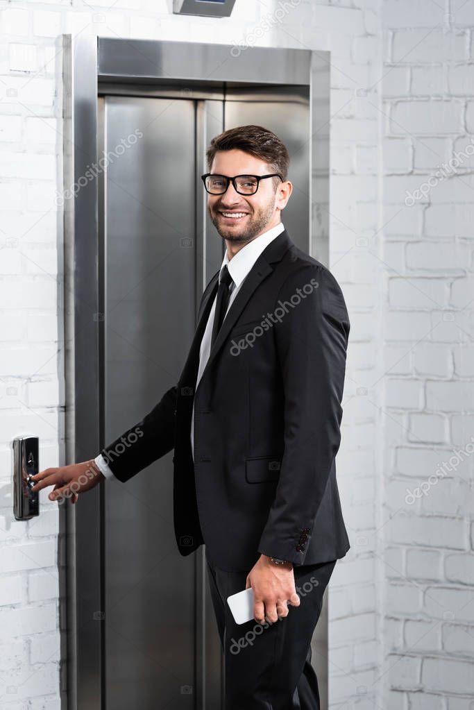 smiling businessman in formal wear pushing button of elevator