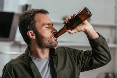 Alkol bağımlısı adam şişeden bira içiyor.