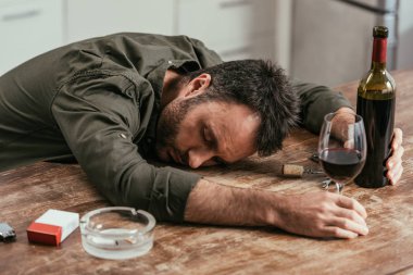 Drunk man sleeping on table with wine and cigarettes clipart