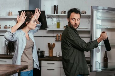 Woman quarreling while husband taking wine bottle from fridge clipart
