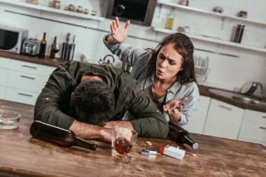 Angry woman quarreling with drunk husband with alcohol addiction on kitchen clipart