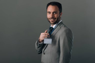 Takım elbiseli gülümseyen adam rozetini tutuyor. Kopya alanı gri renkte.