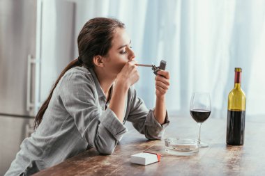 Woman smoking cigarette with wine on kitchen table clipart