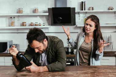 Mutfakta şarap şişesiyle alkol bağımlısı koca kavgası yapan endişeli bir kadın.