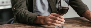 Cropped view of man holding wine glass at table, panoramic shot clipart