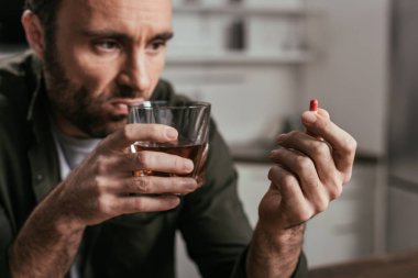 Selective focus of man with alcohol depended holding whiskey glass and pill clipart