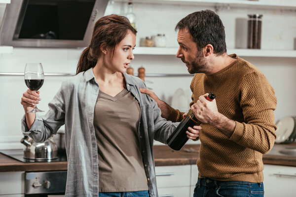 Woman holding wine and quarreling with husband on kitchen