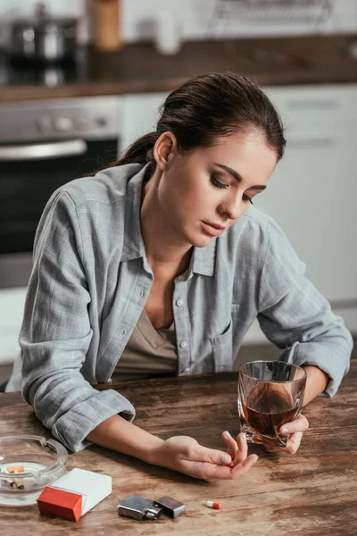 Mulher Preocupada Segurando Copo Uísque Pílulas Mesa Cozinha — Fotografia de Stock