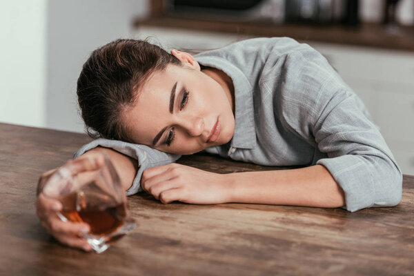 Selective focus of sadness woman holding whiskey glass at table