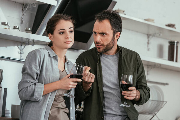 Зависимая от алкоголя пара с бокалами вина ссорятся на кухне
