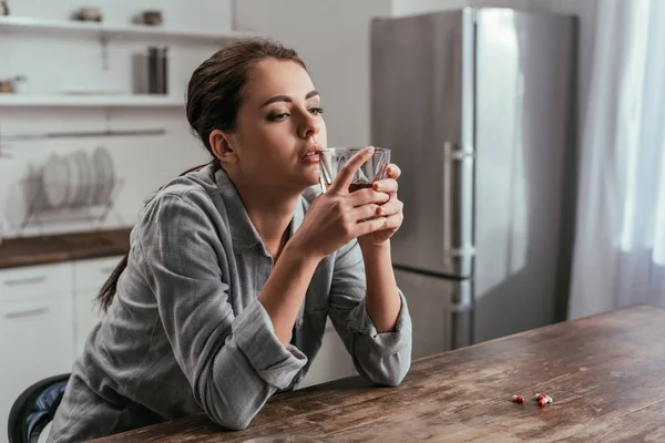 Mulher Deprimida Segurando Copo Uísque Lado Pílulas Mesa — Fotografia de Stock