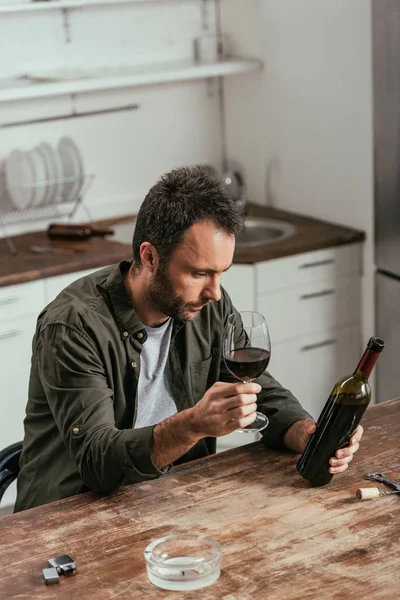 Mann Hält Weinglas Und Flasche Neben Aschenbecher Auf Küchentisch — Stockfoto