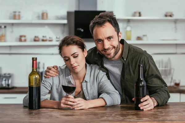 Sorrindo Homem Com Cerveja Abraçando Mulher Triste Com Vinho Cozinha — Fotografia de Stock