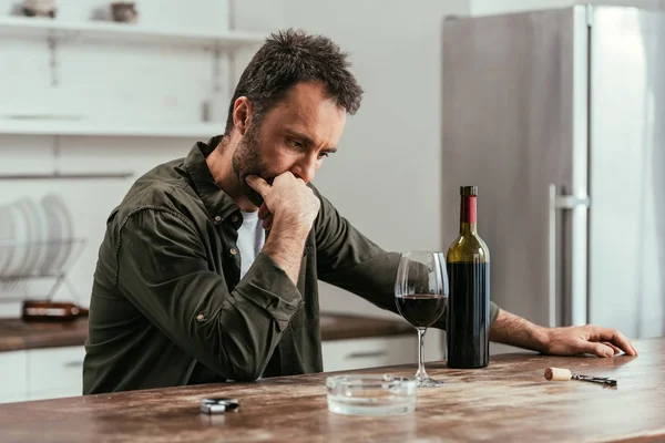 Σκεπτικός Άνθρωπος Κοιτάζοντας Ποτήρι Κρασιού Και Μπουκάλι Στο Τραπέζι Της — Φωτογραφία Αρχείου