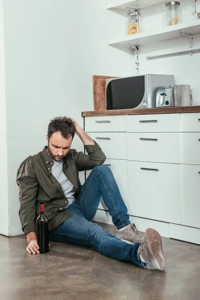Mutfakta şarap şişesiyle oturan üzgün adam.