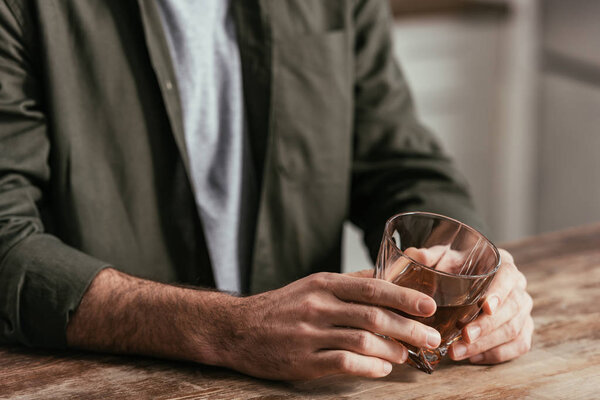 Обрезанный вид человека, держащего стакан виски за столом
