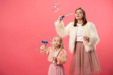 daughter and smiling mother blowing soap bubbles on pink background  clipart