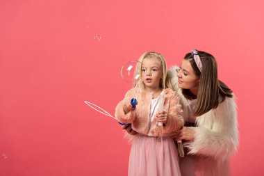 Kızım ve gülümseyen annem pembe sabun köpükleri üflüyorlar.