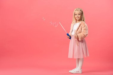 Şirin ve gülümseyen bir çocuk pembe arka planda sabun köpükleri olan bir şişe tutuyor. 